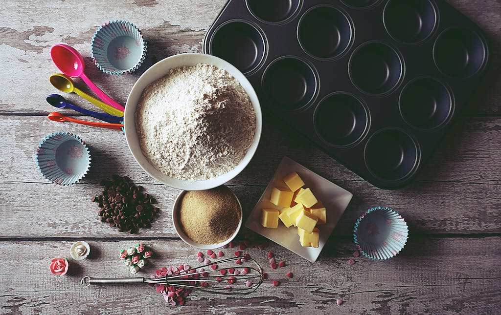 Flat lay of baking ingredients and tools for making cupcakes, including flour, butter, and chocolate chips.
