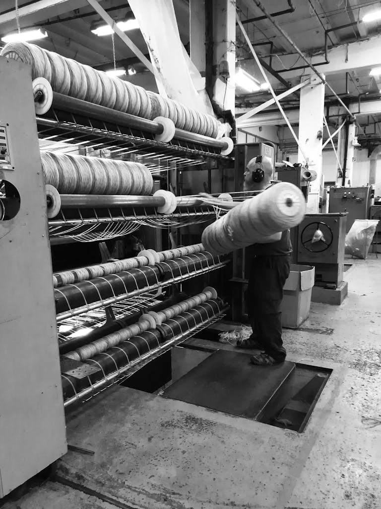 Black and white image of a man working in a textile factory operating machinery.