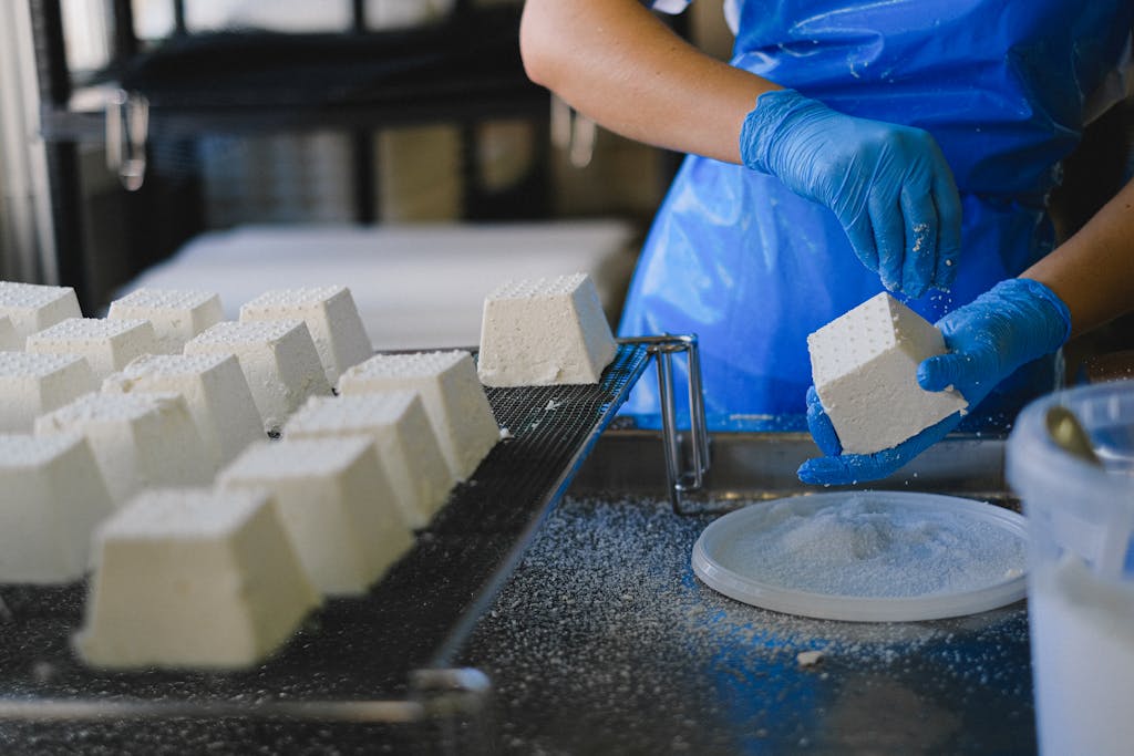 Midsection of a factory worker preparing cheese blocks with blue gloves in an industrial dairy setting.